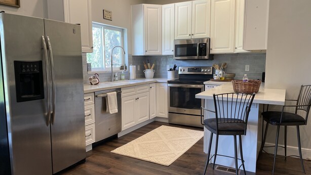 A modern kitchen with stainless steel appliances, white cabinetry, and a central island with bar stools. - Guest Apartment close to Ski Resorts, Hiking Trails, Shopping Restaurants & more (Holladay)