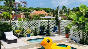 Uma piscina com um pato de borracha amarelo, uma espreguiçadeira e uma mesa com cadeiras.