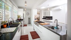 Uma cozinha moderna com armários brancos, uma ilha central, eletrodomésticos de aço inoxidável e iluminação pendente.