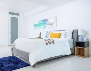 A modern bedroom with a bed, bedside tables, a blue rug, and a painting on the wall. - Mansion Laura - a master room for everyone. (Guaynabo)