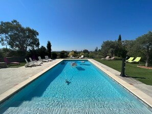 Une piscine rectangulaire à l’eau d’un bleu cristallin, entourée de chaises longues et d’un mur en pierre.