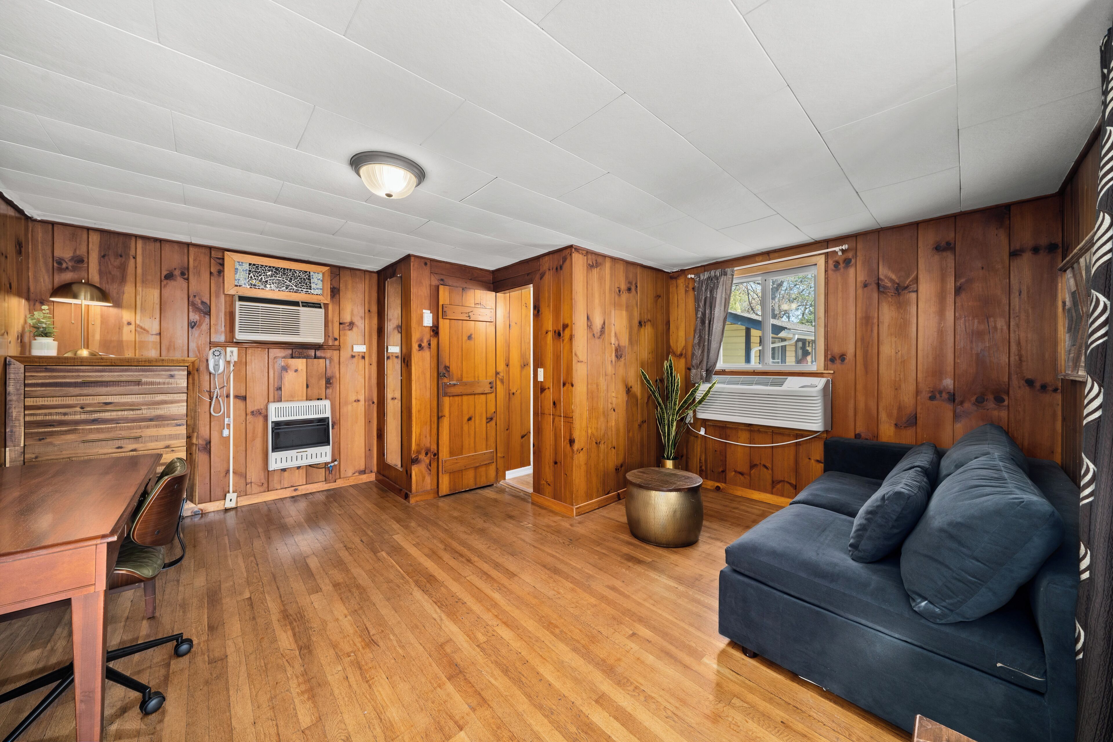 A room with wooden walls and floors, a sofa, a table, and a potted plant.