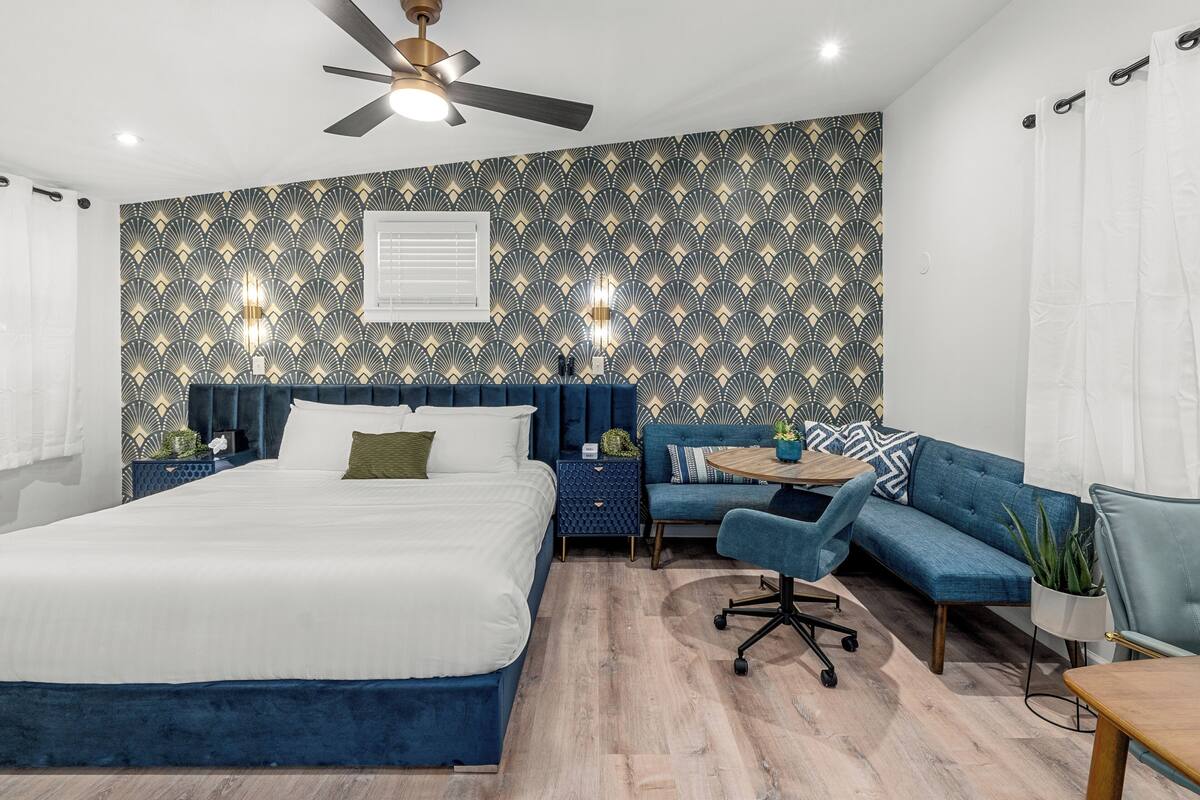 A modern bedroom with a large bed, a blue sofa, a small round table, and a ceiling fan.