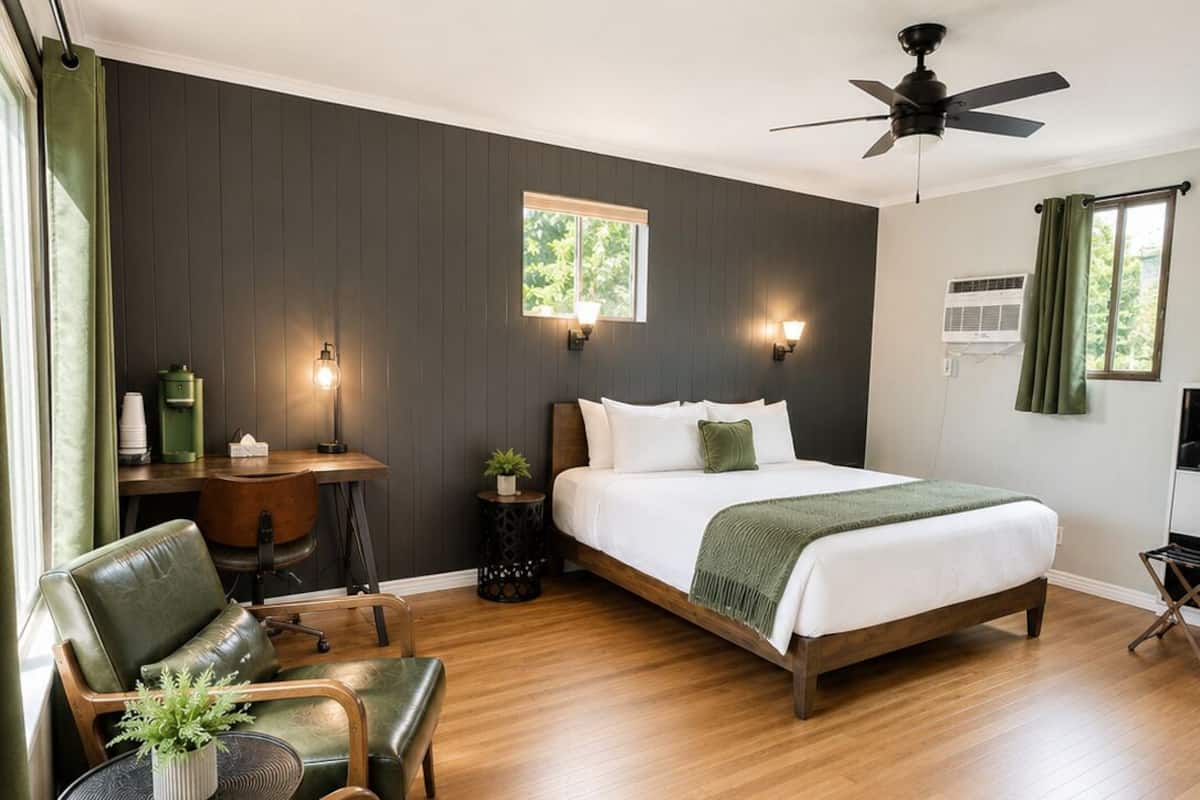 A bedroom with a bed, a desk, a chair, a ceiling fan, and a window.