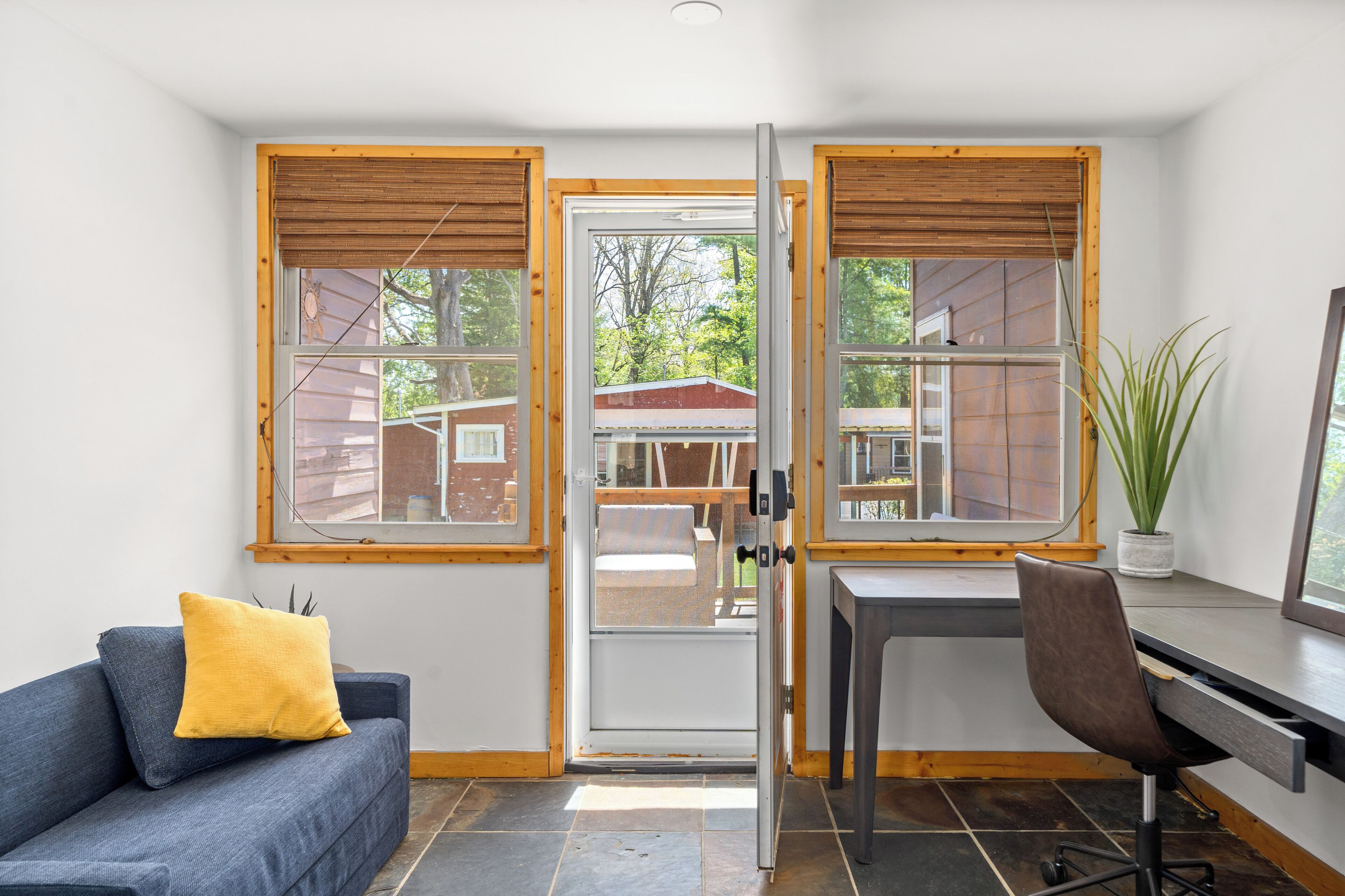 A room with a desk, a chair, a sofa, and a large window with wooden shutters.