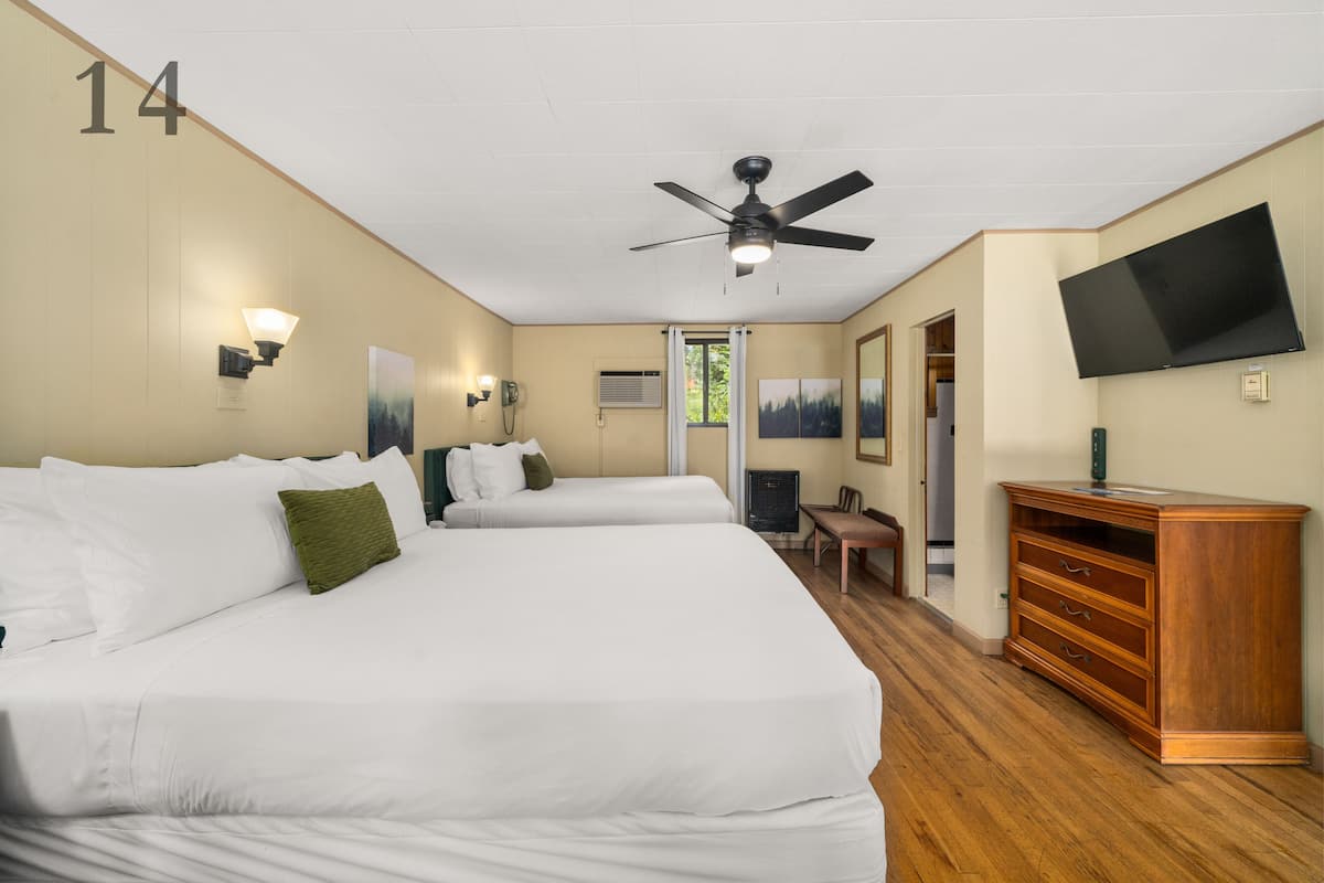 A hotel room with two beds, a ceiling fan, a flat-screen TV, a wooden dresser, and a desk with a chair.