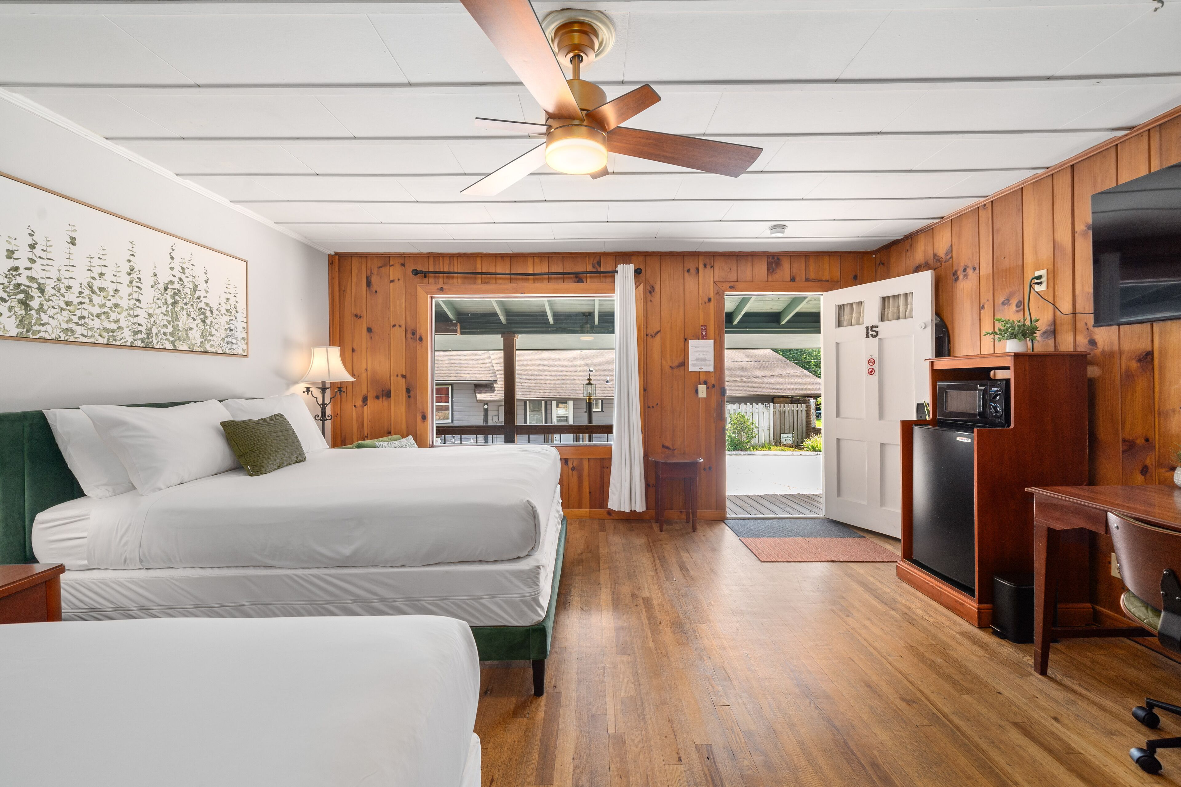 A hotel room with two beds, a ceiling fan, a TV, and a wooden interior.