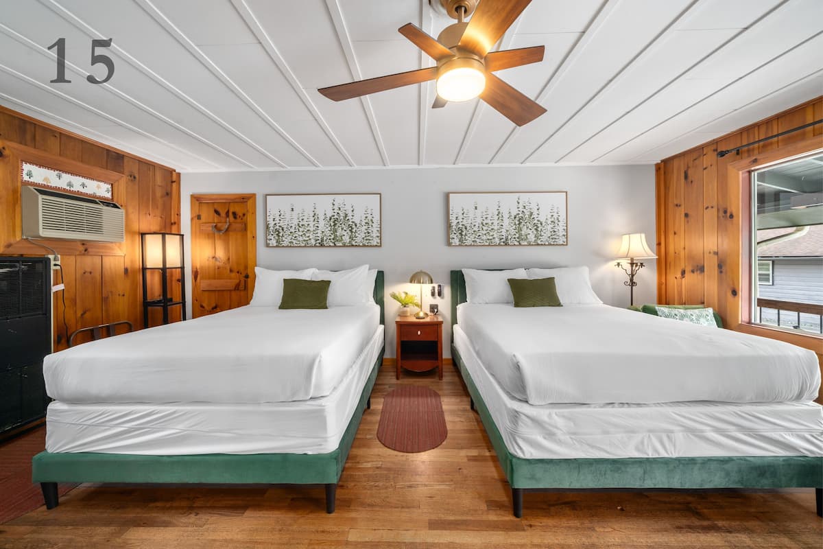 A hotel room with two beds, wooden walls, a ceiling fan, and a large window.