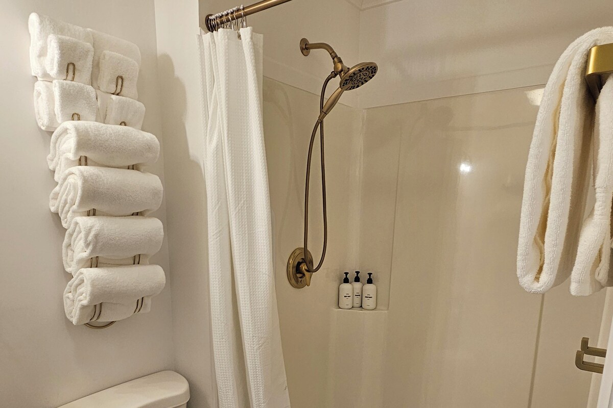 A bathroom with a toilet, a shower with a glass door, and a towel rack with towels.