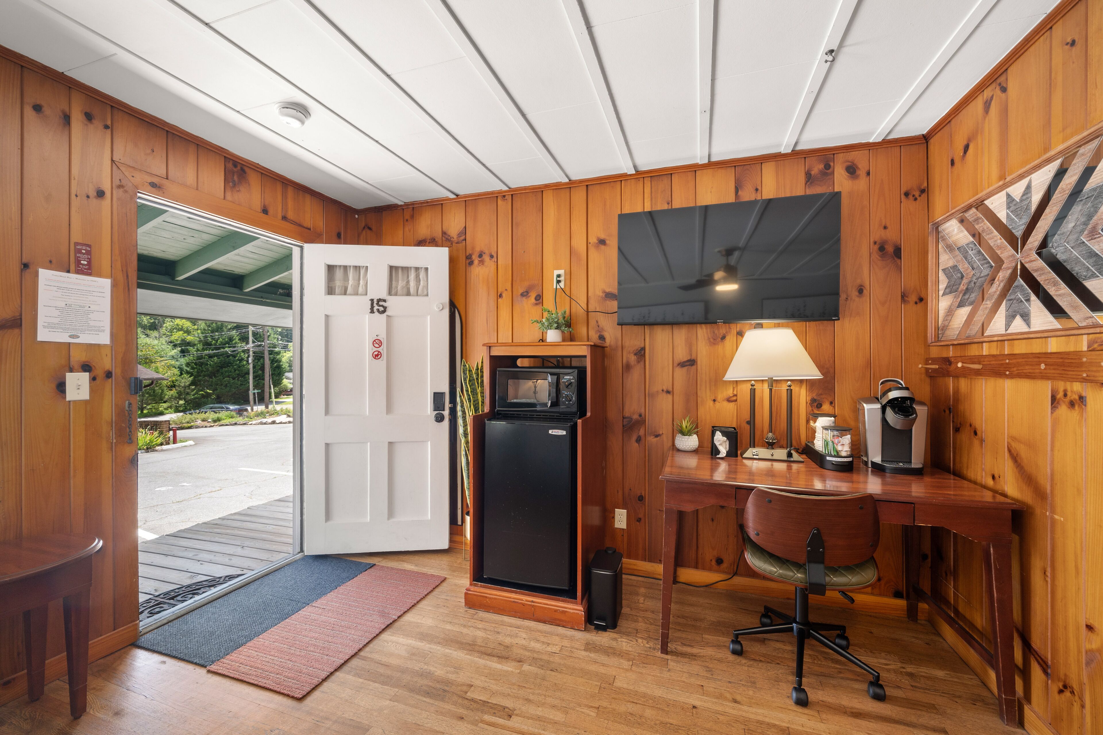 Une pièce aux murs lambrissés, comprenant un bureau, une chaise, un four à micro-ondes et une porte donnant sur l’extérieur.