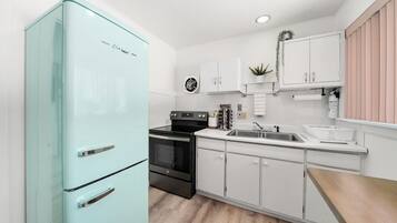 Een moderne keuken met een blauwgroene koelkast, een zwarte kookplaat, witte kastjes en een houten aanrecht.