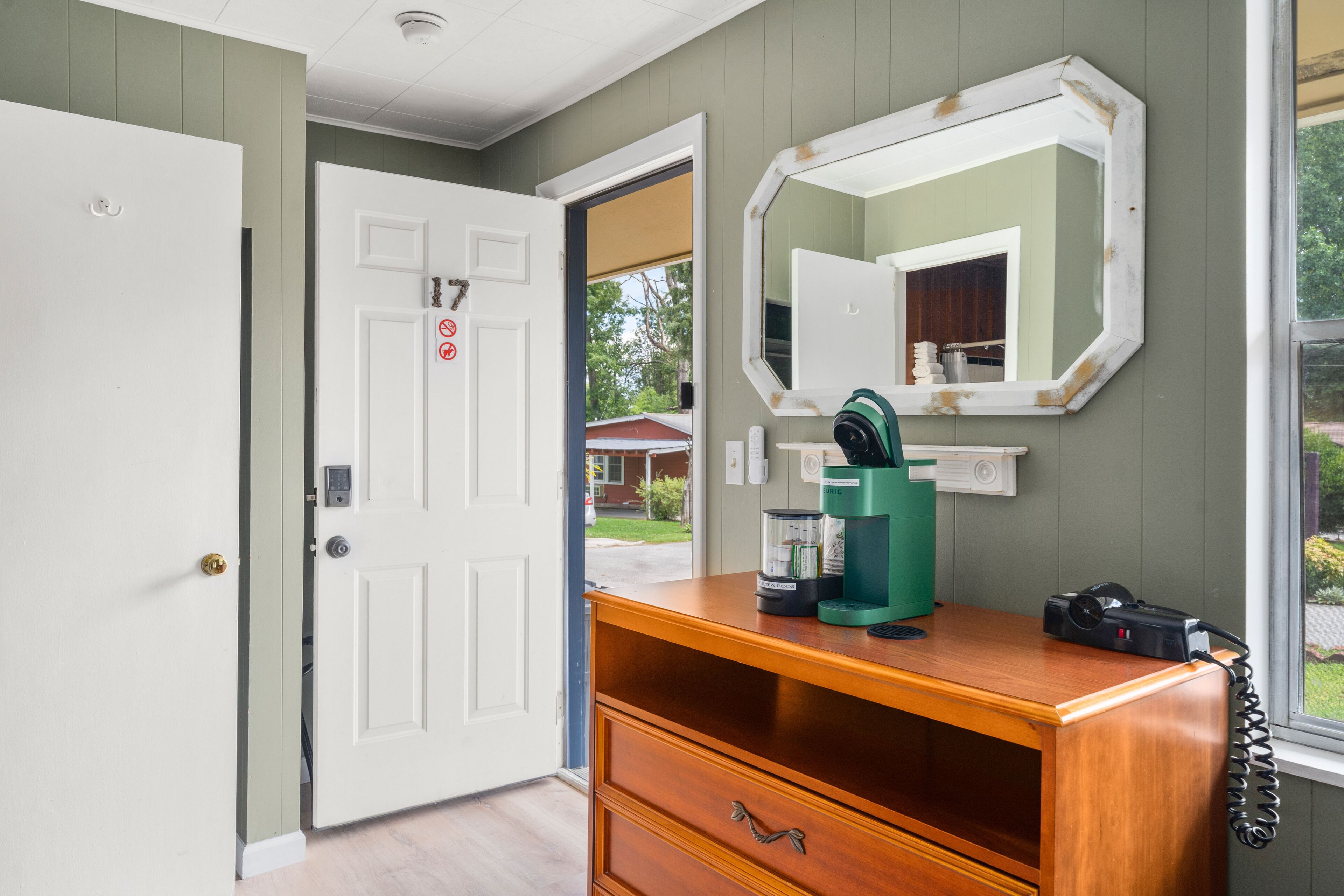 A room with a wooden dresser, a coffee maker, a telephone, and a mirror on the wall.