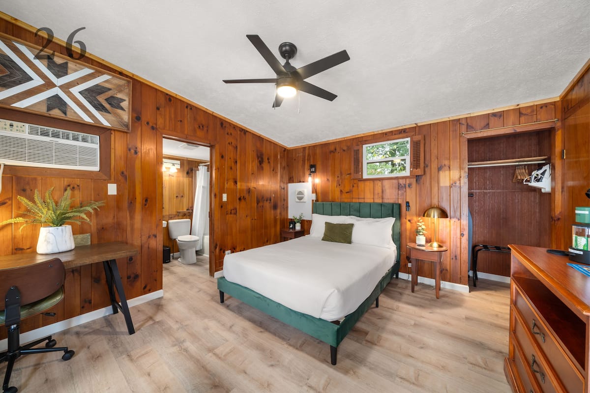 A bedroom with a bed, desk, chair, and a ceiling fan.