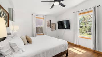 A bedroom with a bed, a ceiling fan, a TV, and large windows with curtains.