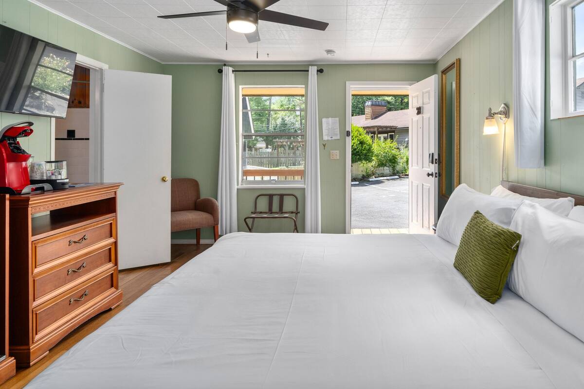 A bedroom with a bed, dresser, chair, and a door leading outside.