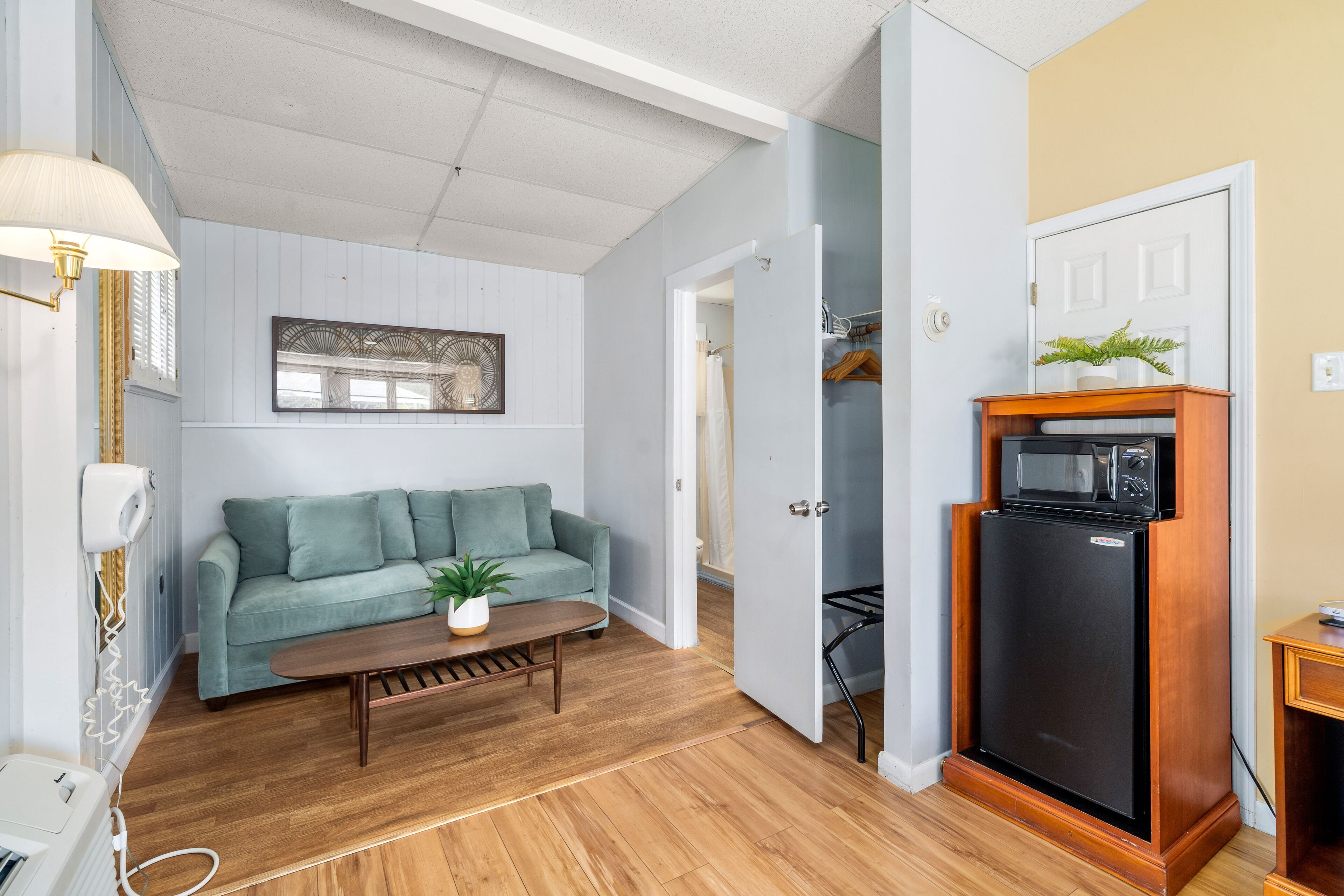 A compact living space with a sofa, a coffee table, a microwave, and a small refrigerator.