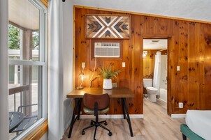 Habitación con pared de paneles de madera, un escritorio con silla, una planta en maceta y vistas al exterior.