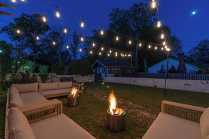 Un patio al aire libre con un hogar para fuego, luces colgantes y un sofá.
