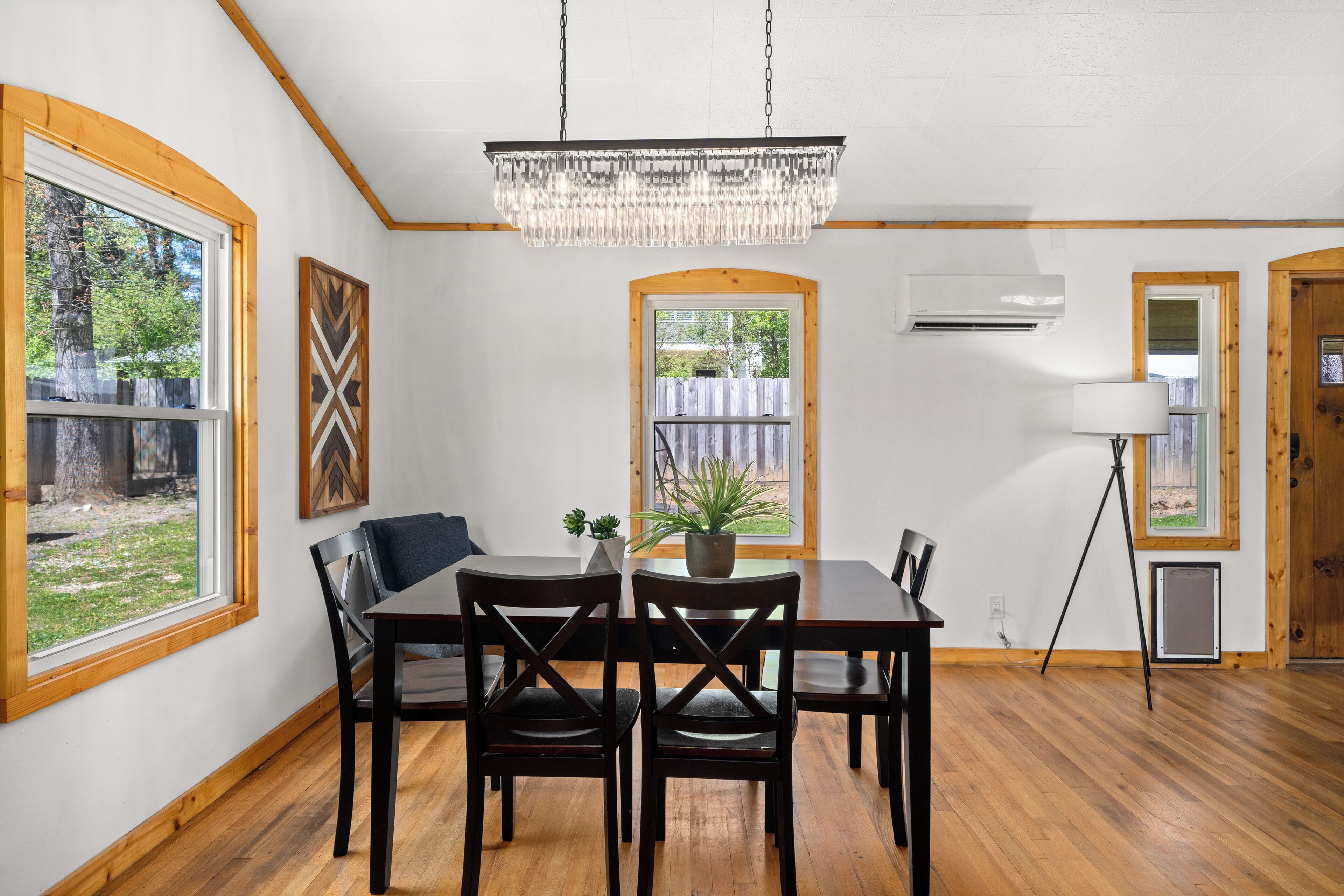 Un espace repas agrémenté d’un lustre, d’un plancher en bois et offrant une vue sur l’extérieur.