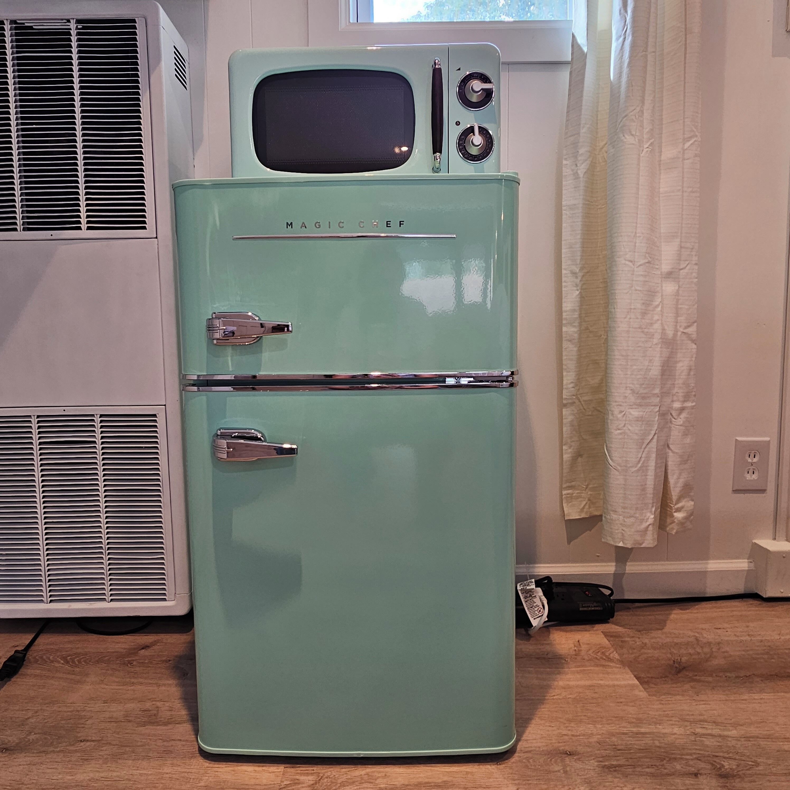 Uma geladeira vintage azul-esverdeada com um micro-ondas em cima, duas portas e um painel de controle com botões.
