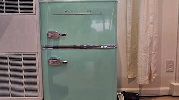 Uma geladeira vintage azul-esverdeada com um micro-ondas em cima, duas portas e um painel de controle com botões.