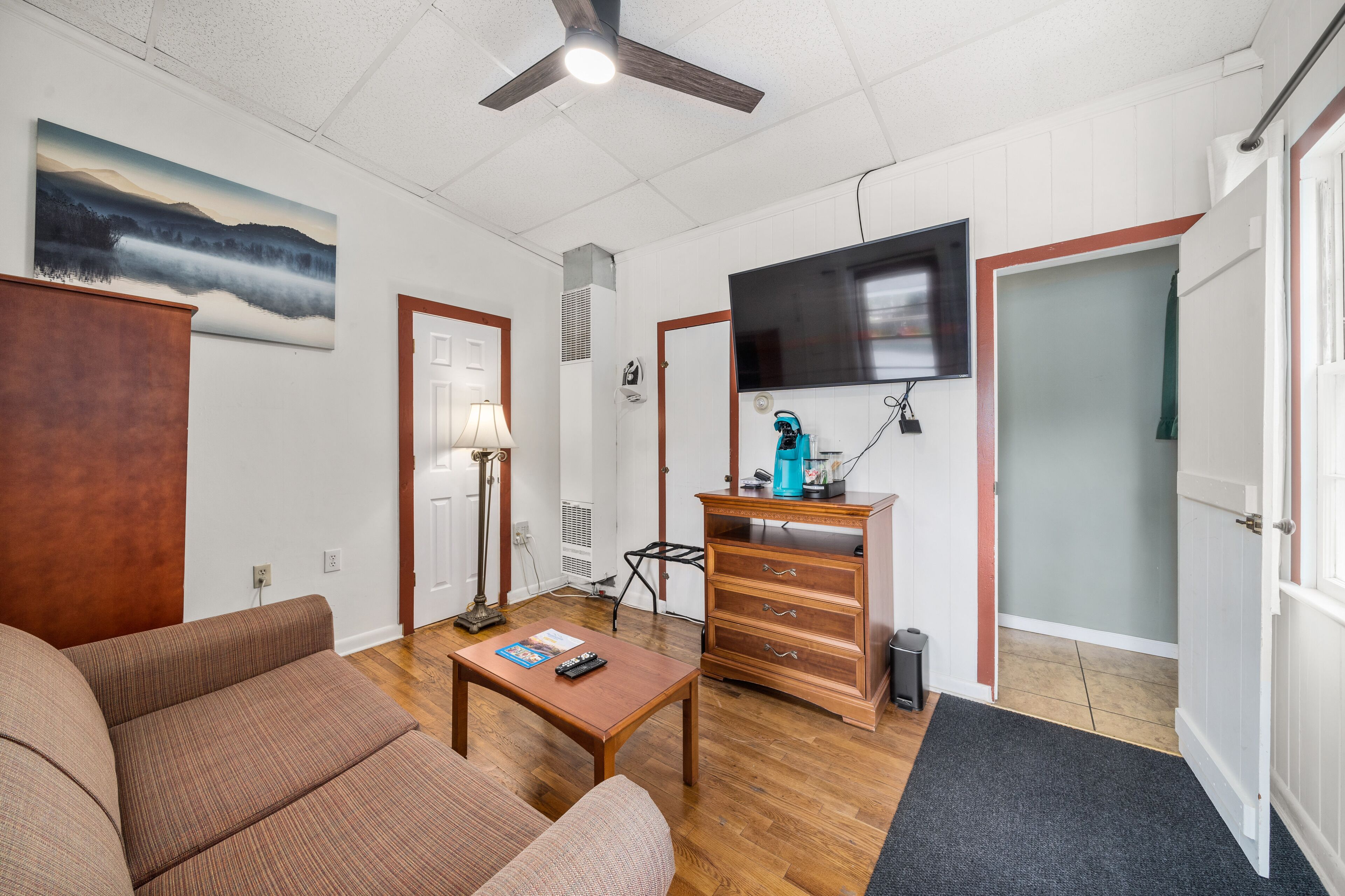 Een woonkamer met een bank, een bijzettafeltje, een televisie aan de muur, een houten kast en een deur.