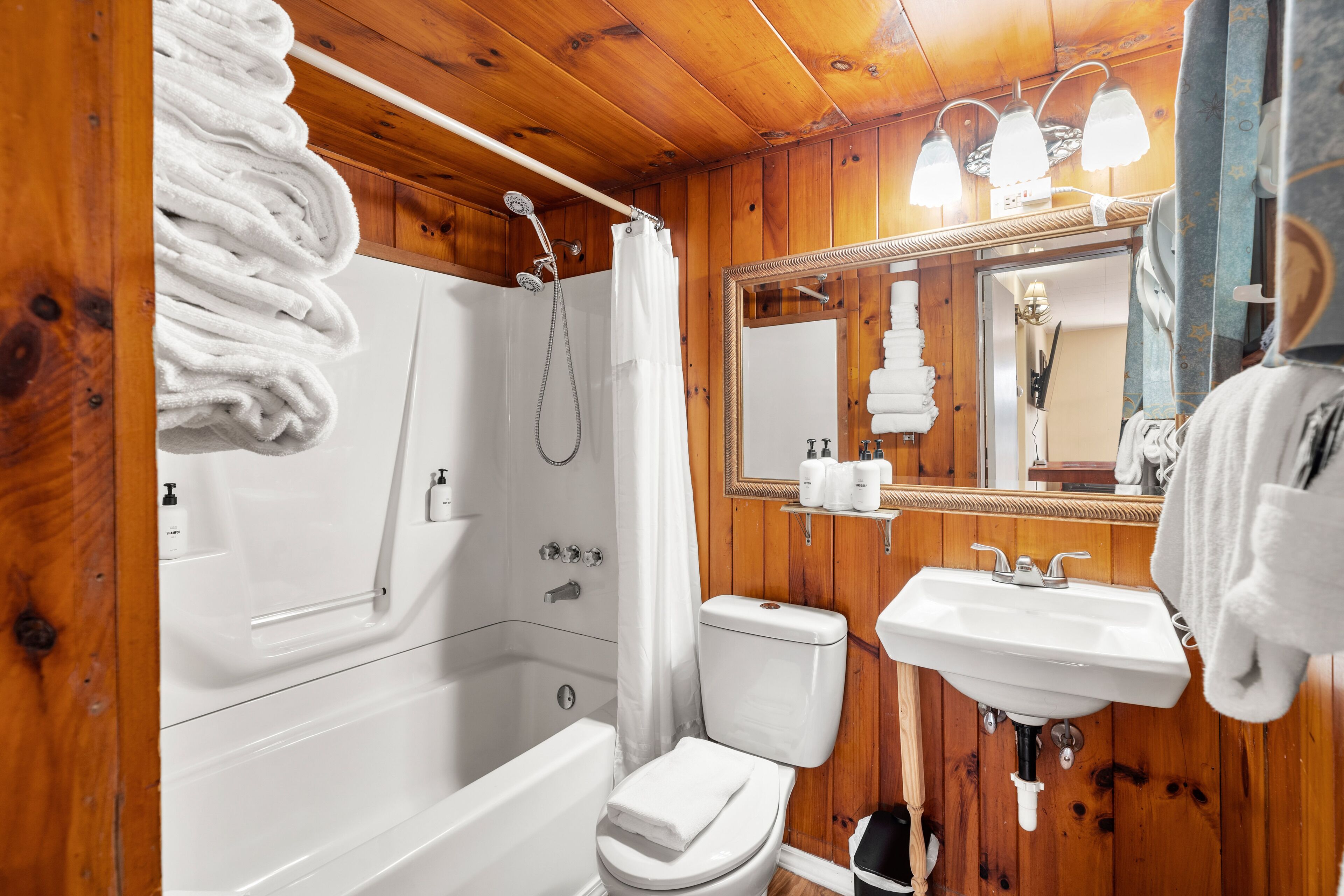 A wooden-paneled bathroom with a bathtub, toilet, and sink.