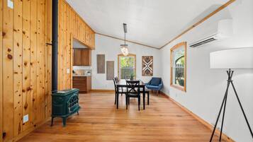 A spacious room with wooden walls, a dining table with chairs, a blue chair, a green stove, and a floor lamp.
