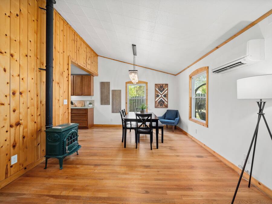 A spacious room with wooden walls, a dining table with chairs, a blue chair, a green stove, and a floor lamp.
