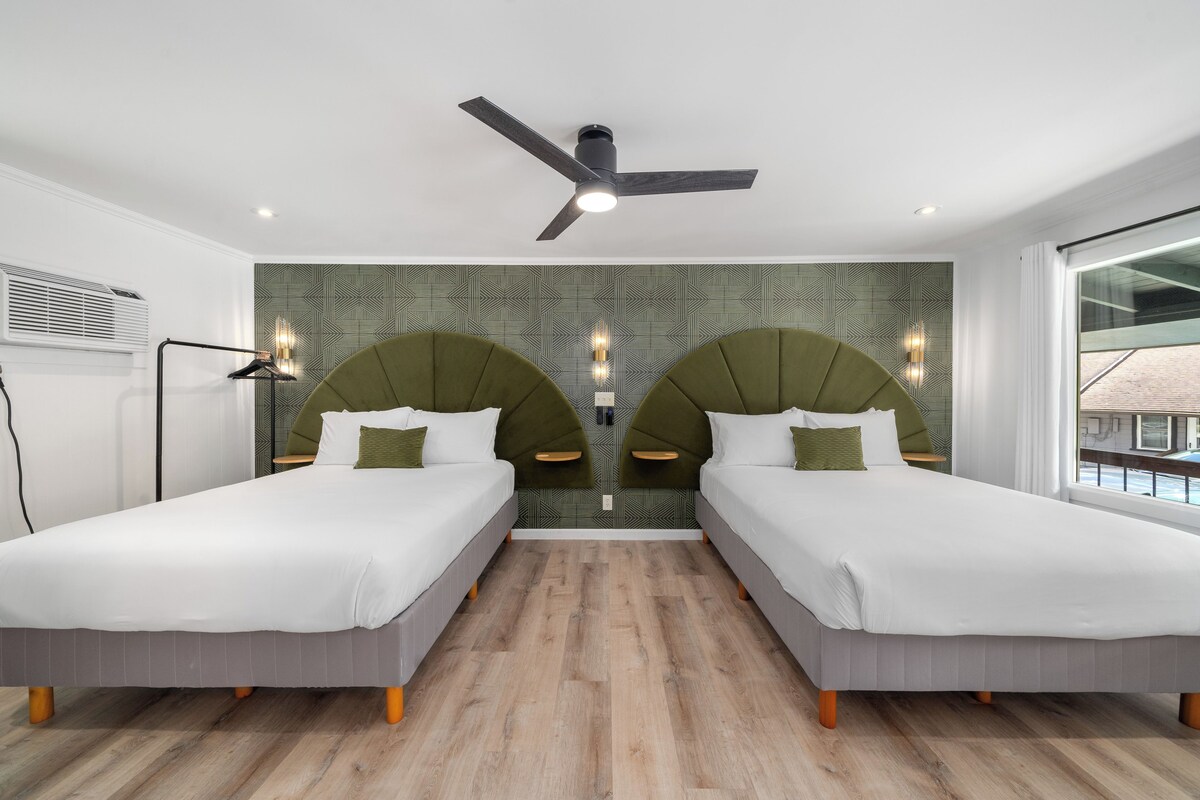 A hotel room with two beds, a ceiling fan, a patterned wall, and a large window.