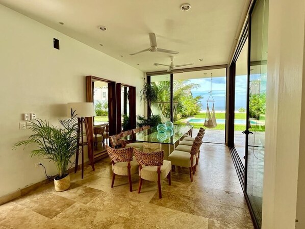 Ein geräumiger Essbereich mit einem Glastisch und Stühlen, einem Deckenventilator und Blick auf ein Schwimmbad und Grünflächen.
