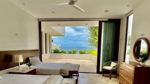 Ein modernes Schlafzimmer mit zwei Betten, einem Deckenventilator und Meerblick.