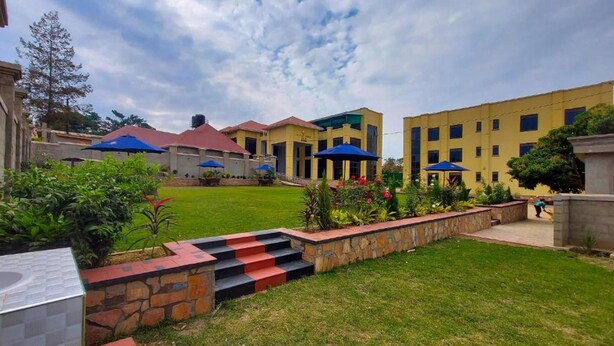 A courtyard with a grassy lawn, steps leading to a building, and outdoor umbrellas. - Golden Castle Hotel (Hoima)