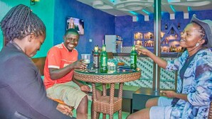 A bar area with a round table, bottles, and glasses. - Golden Castle Hotel (Hoima)