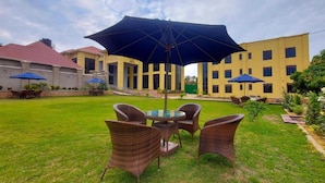 A courtyard with a round table and four wicker chairs, surrounded by a well-maintained lawn. - Golden Castle Hotel (Hoima)