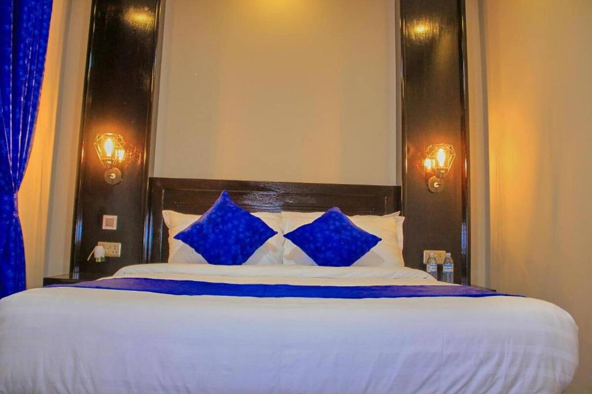 A hotel room with a large bed, two blue pillows, and wall-mounted light fixtures.