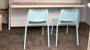 Ein Zimmer mit einem weißen Schrank, zwei hellblauen Stühlen und einem Holztisch.