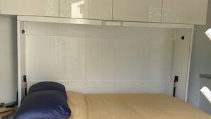 Ein Bett mit weißem Gestell, einer beigen Matratze und zwei Kissen, eines blau und eines beige.
