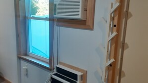 Ein Zimmer mit Fenster, Klimaanlage, Wandregal und Tür.