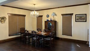 A dining room with a wooden table and chairs, a chandelier, and large windows with blinds. - 1920s Farmhouse  (Wichita Falls)
