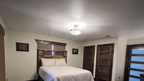 A bedroom with a bed, a wooden headboard, a ceiling light, and a patterned rug. - 1920s Farmhouse  (Wichita Falls)