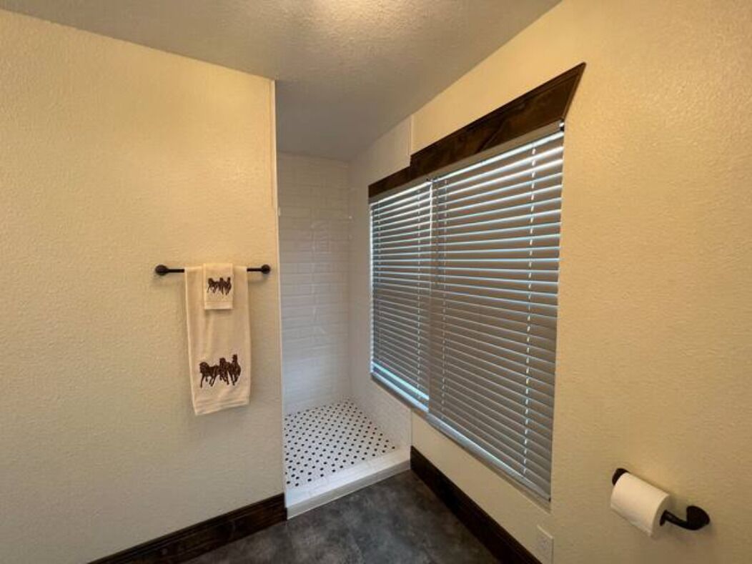 A bathroom with a toilet, a towel rack with towels, a window with blinds, and a shower area.