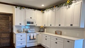 A kitchen with white cabinets, a wooden door, and a countertop with a toaster and kettle. - 1920s Farmhouse  (Wichita Falls)