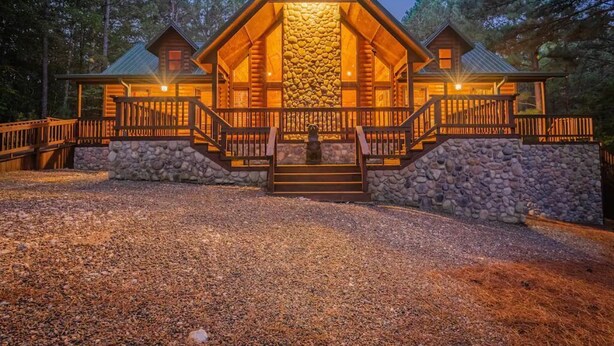 A log cabin with a stone facade, wooden deck, and a gravel driveway. - Deer Ridge Cabin - Hochatown - Hot Tub - Firepit - Spacious Deck - Large Yard (Broken Bow)