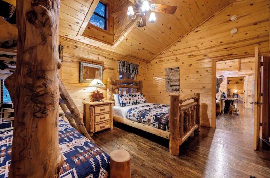 A log cabin bedroom with a bed, nightstands, and a wooden tree trunk.