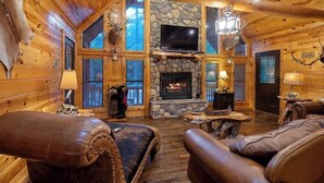 A log cabin interior with a stone fireplace, leather furniture, and mounted animal heads. - Deer Ridge Cabin - Hochatown - Hot Tub - Firepit - Spacious Deck - Large Yard (Broken Bow)
