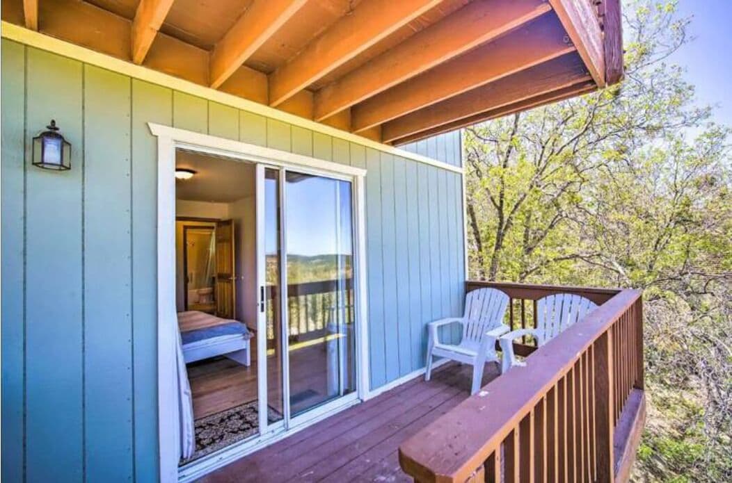 Une terrasse en bois avec une porte-fenêtre coulissante donnant accès à une chambre équipée d’un lit et d’une table de chevet.