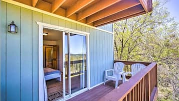 A wooden deck with a sliding glass door leading to a bedroom with a bed and a nightstand.