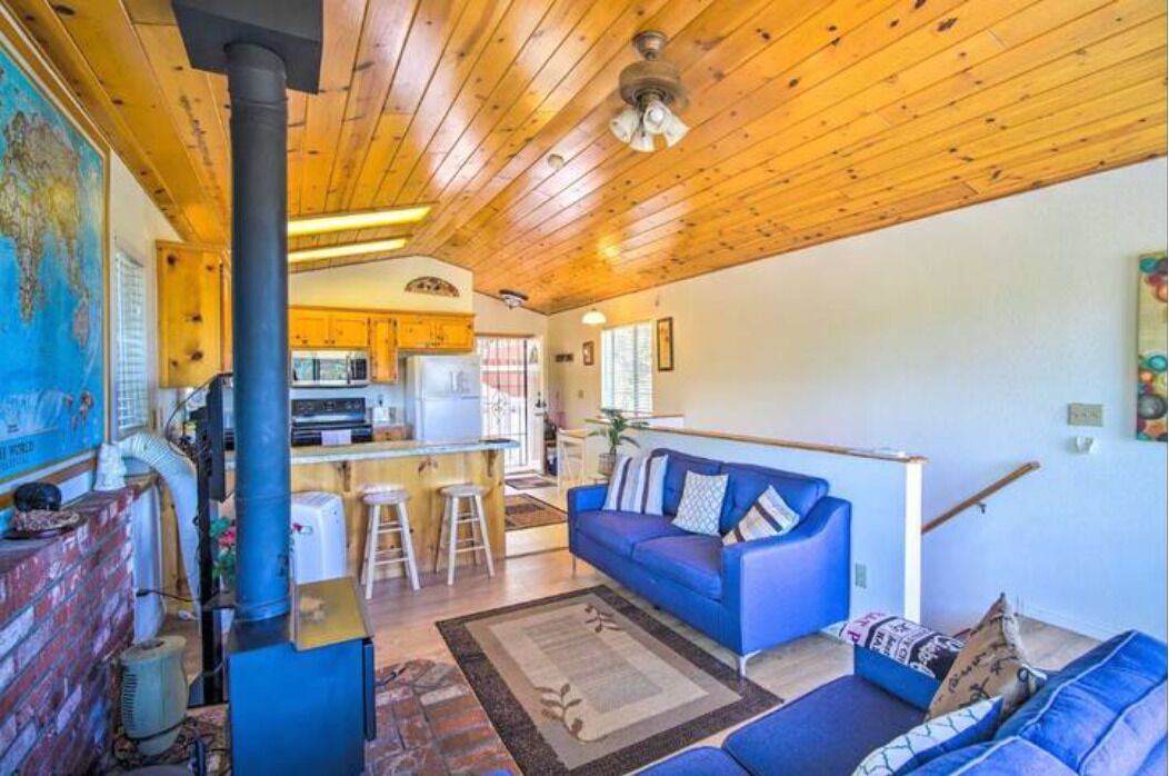 Interior acogedor de una cabaña con techo de madera, un sofá azul, una zona de cocina y un mapa grande en la pared.