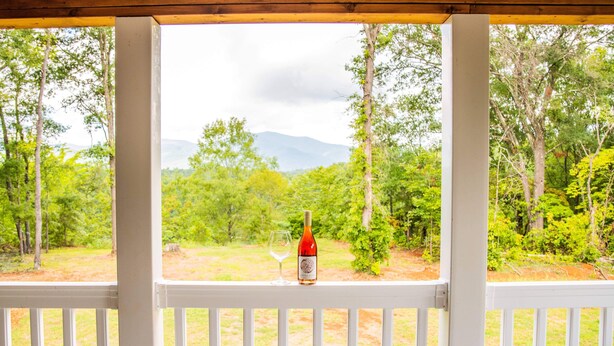 A bottle of wine and a glass on a white railing with a view of a forest and mountains. - JULY DISCOUNT! Romantic 2 BR 2 story w/mountain views and stunning outdoor space (Amherst)